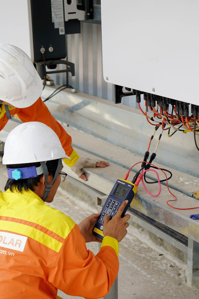 Two electrical engineers installing and testing solar power systems wearing safety gear at a construction site.
